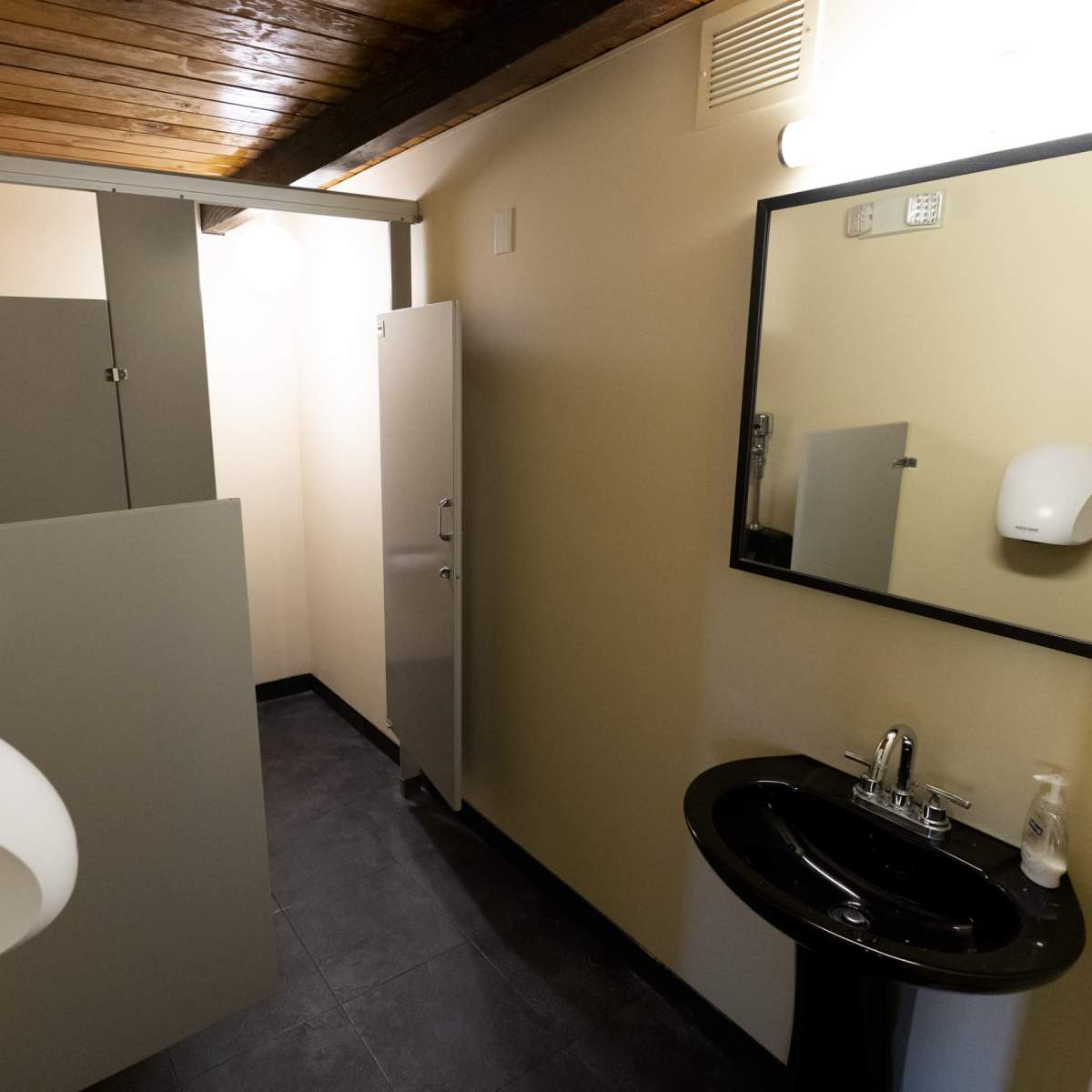 A minimalist bathroom with a sink and two stalls enclosed by gray partitions.