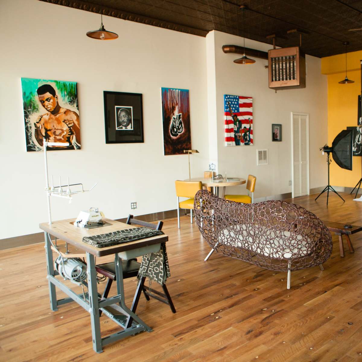 An artist studio with a wooden floor, featuring a large backdrop, photography equipment, and various artworks on the walls.