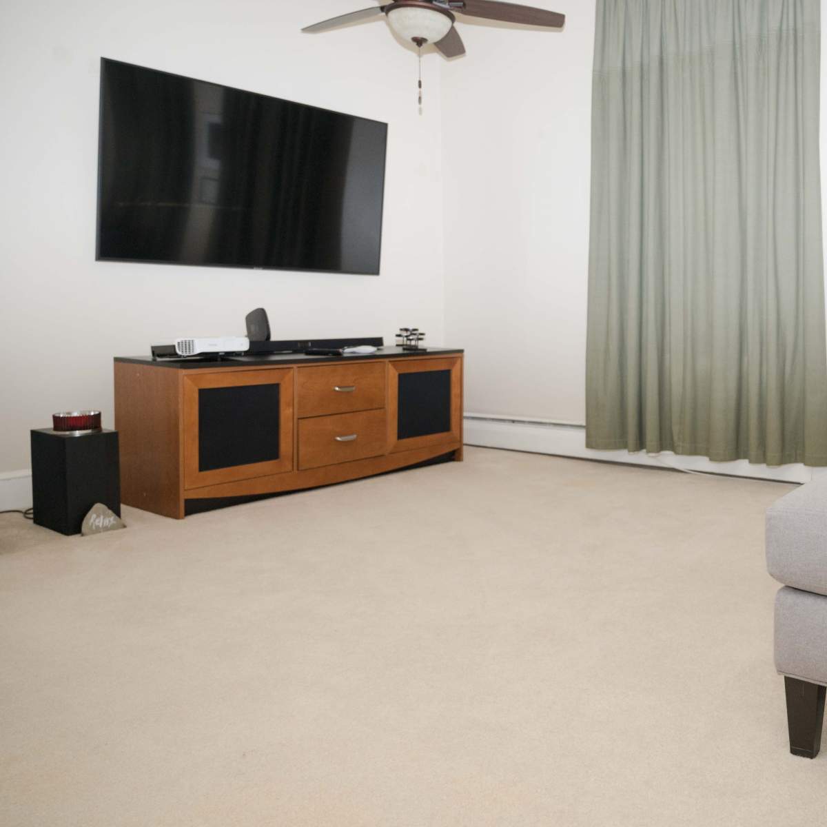 A living room with a television mounted on the wall, a wooden entertainment unit, and a gray sofa with cushions on a beige carpet.
