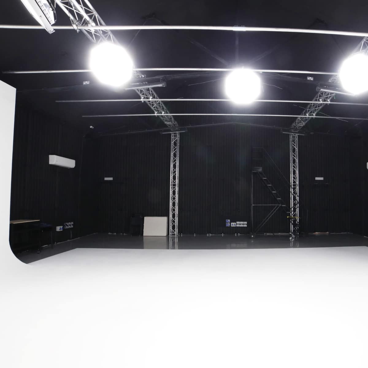 An empty studio space with a white backdrop, overhead lights, and black walls.