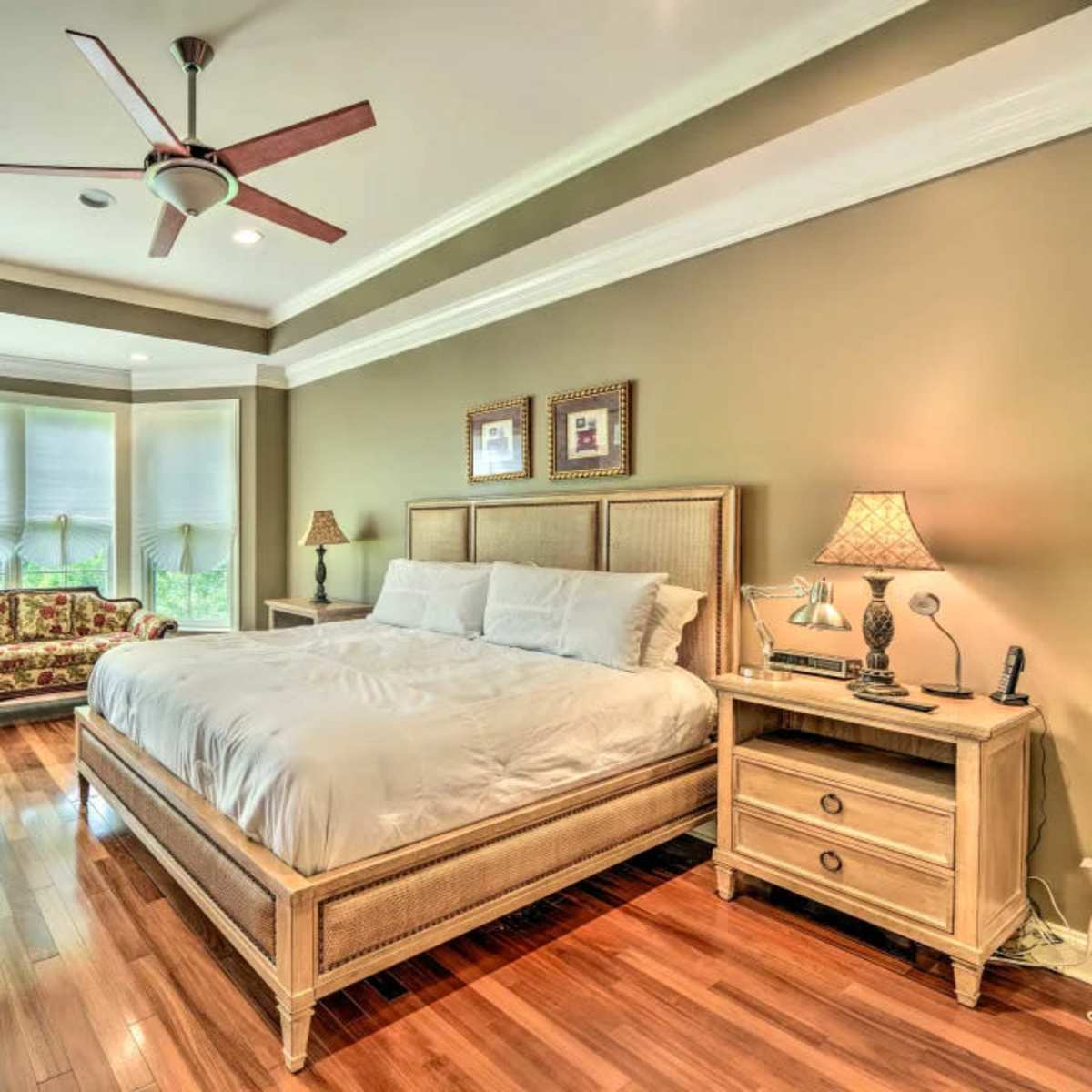A well-furnished bedroom featuring a large bed, a dresser, a bedside table, and a decorative seating area with a mirror against the wall.