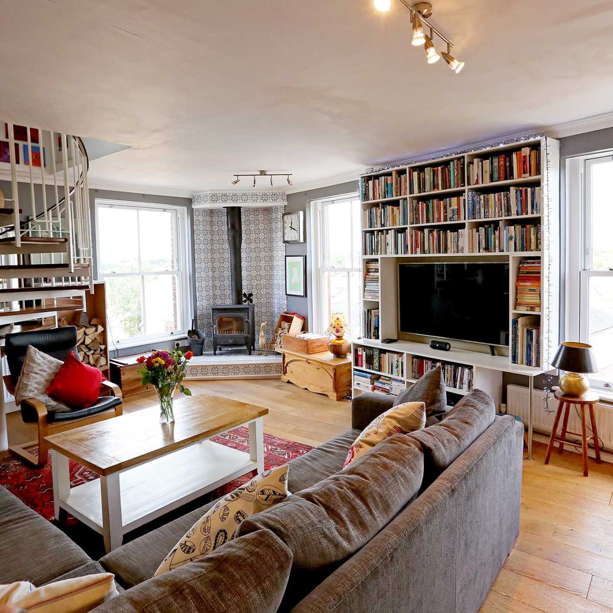 The living room features a gray sectional sofa, a wooden coffee table, built-in bookshelves, a spiral staircase, large windows, and a fireplace.