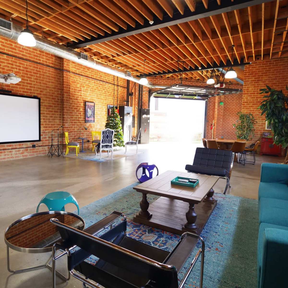 An industrial-style interior with exposed brick walls, a large white screen, and various seating arrangements.