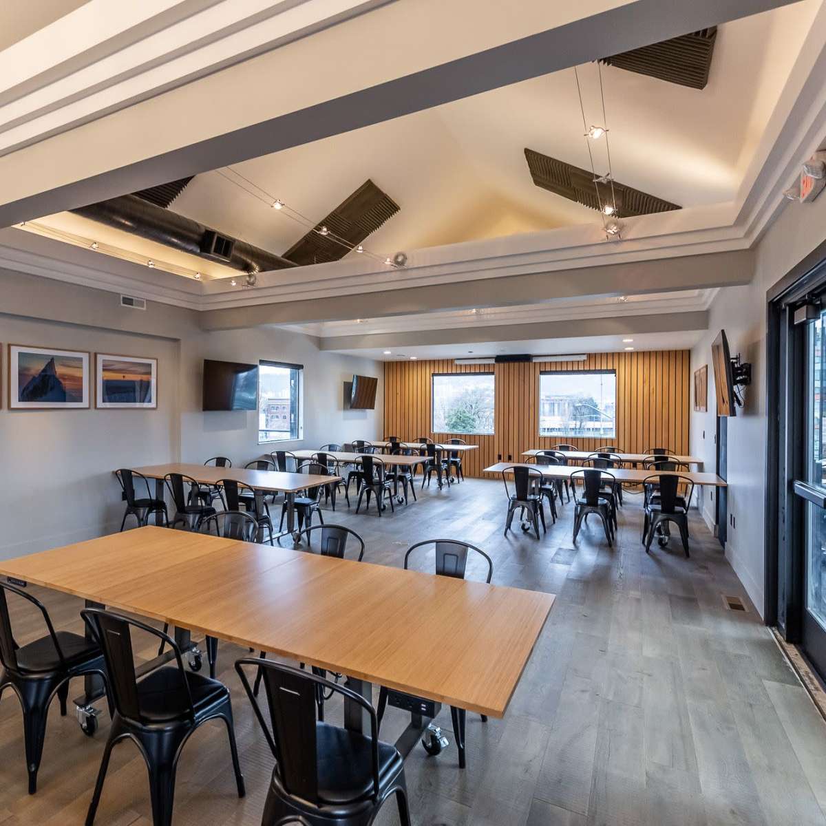 The interior of a spacious restaurant features several tables arranged neatly under a ceiling with modern design elements and large windows that provide natural light.