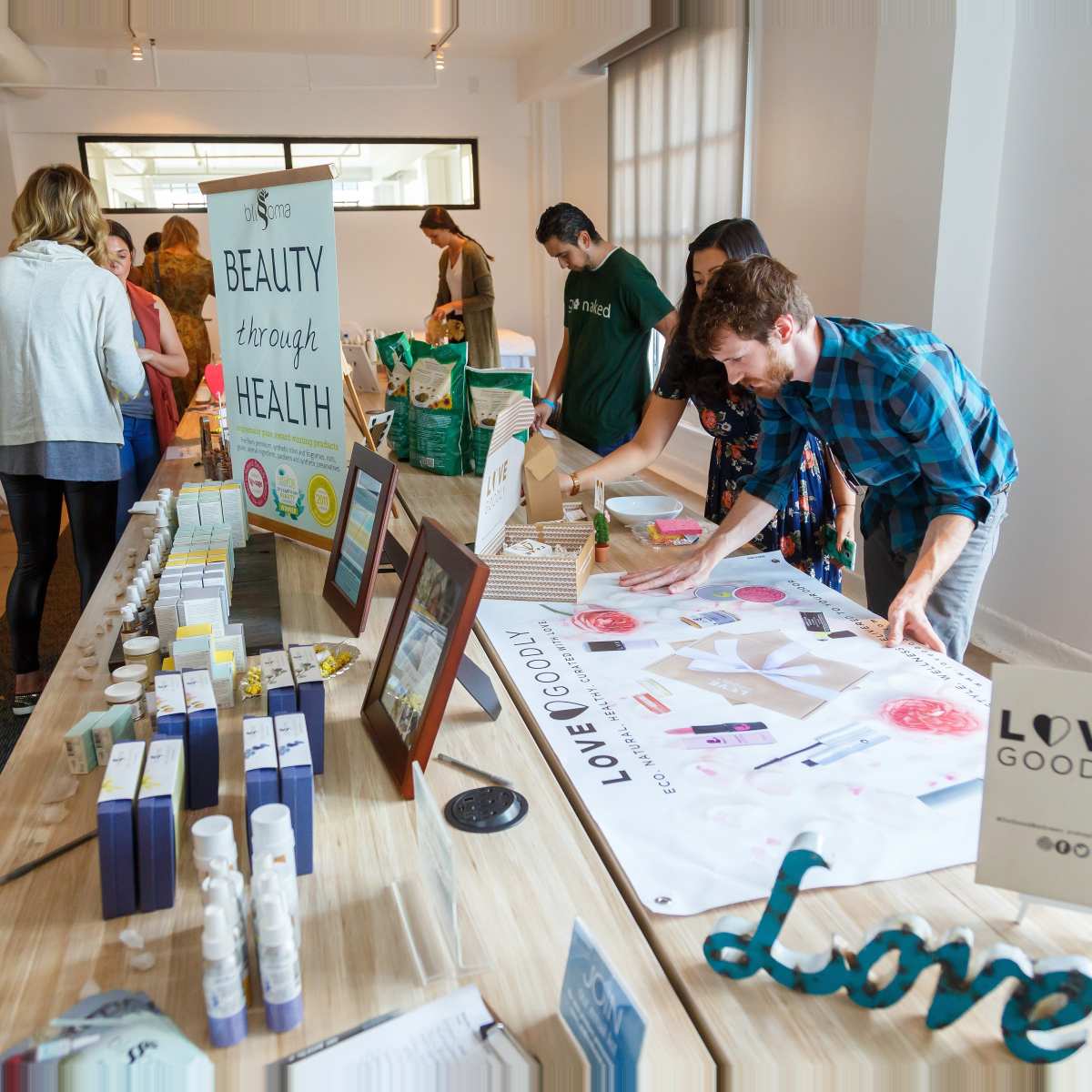 A group of people interacting at a health and wellness event with a long table featuring various products and informational materials.