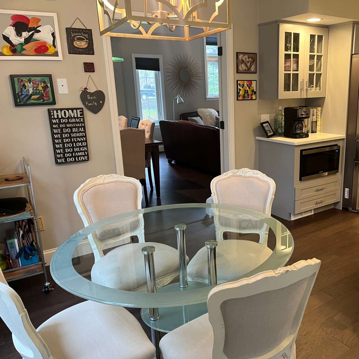A modern kitchen area with a glass dining table surrounded by upholstered chairs, alongside a stainless steel refrigerator and a countertop with a microwave.