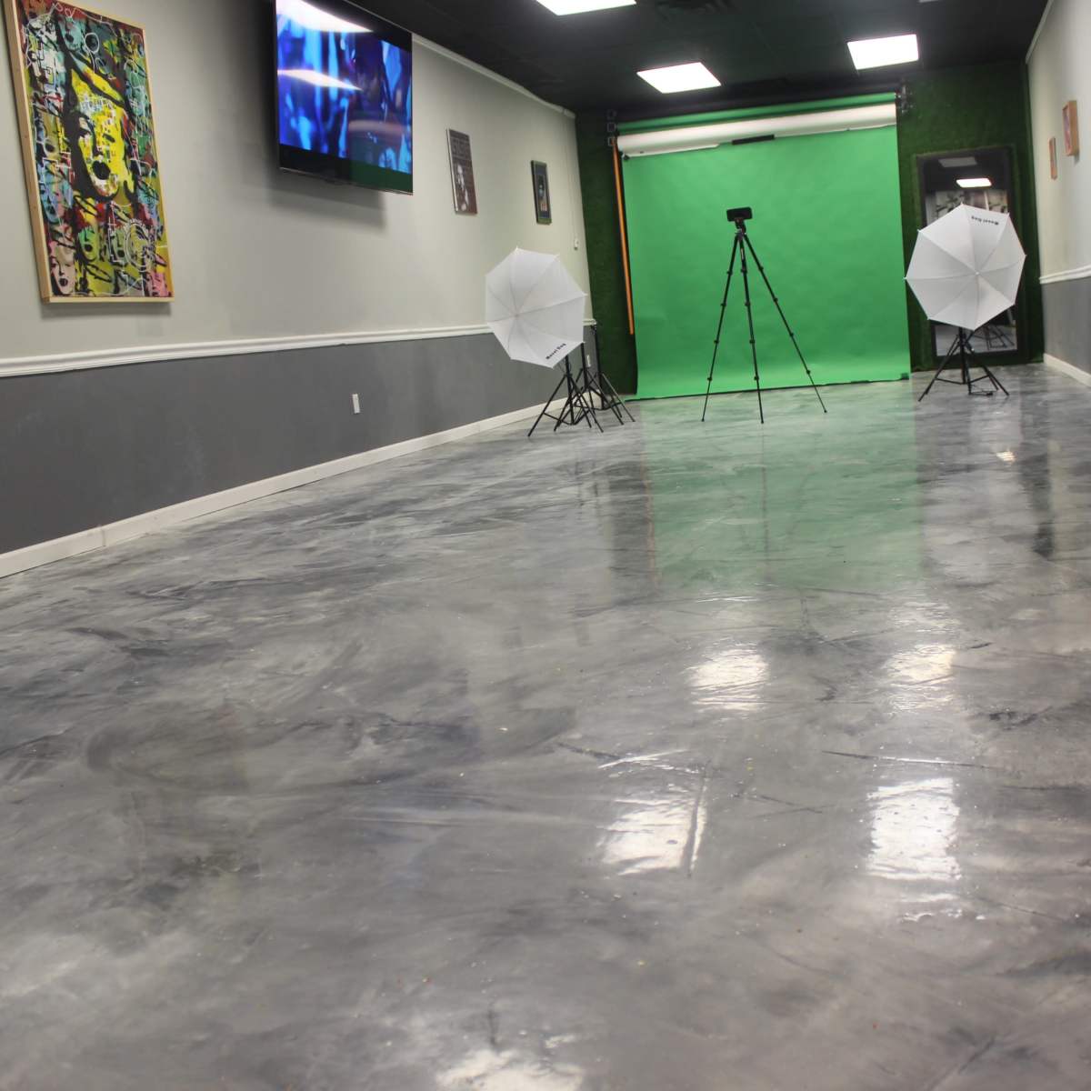 A spacious room with a polished concrete floor, two white umbrella lights set up on tripods, and a green backdrop along one wall.