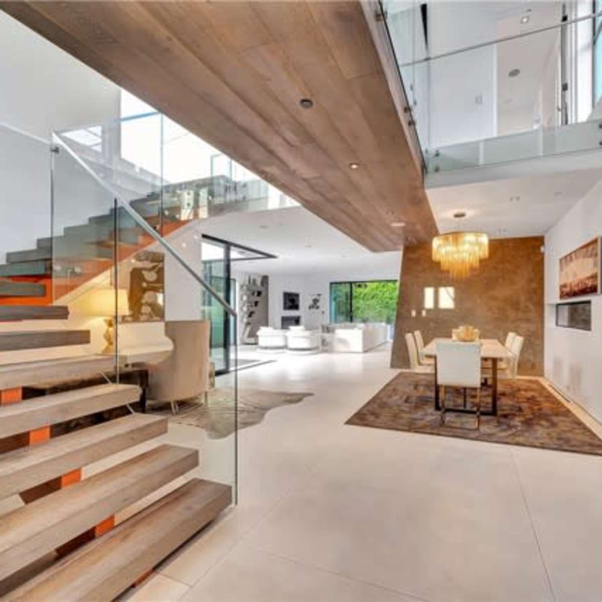 A modern open-concept living space with a staircase, dining area, and large windows allowing natural light.