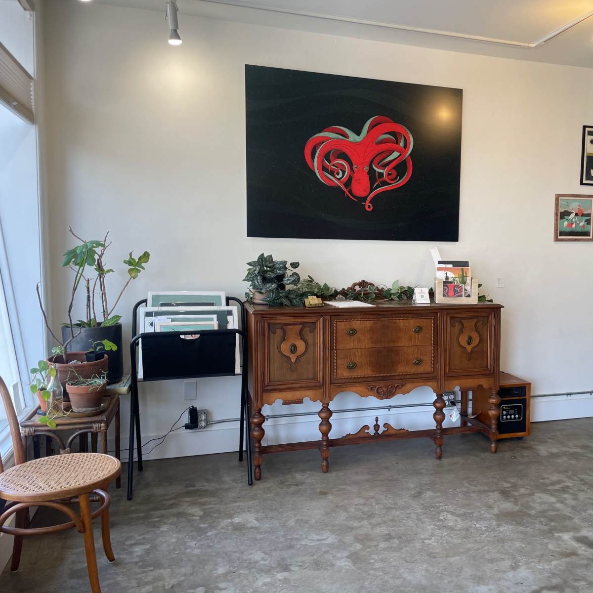 A room with a wooden sideboard against the wall, decorated with plants and a variety of framed artworks.