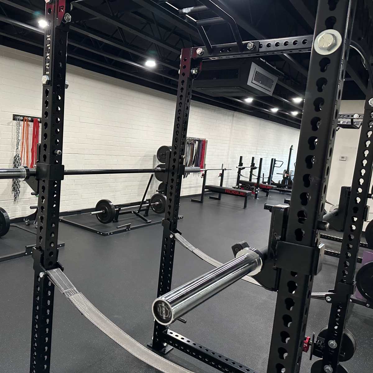 A well-equipped gym space featuring a squat rack, barbells, and weight plates on the floor.