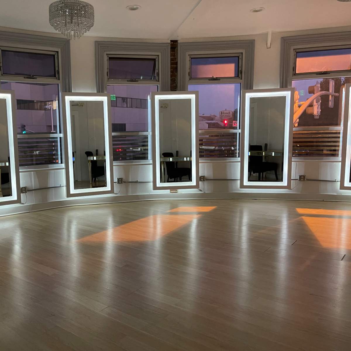 A room with five illuminated mirrors surrounded by large windows, reflecting the soft light of the setting sun.