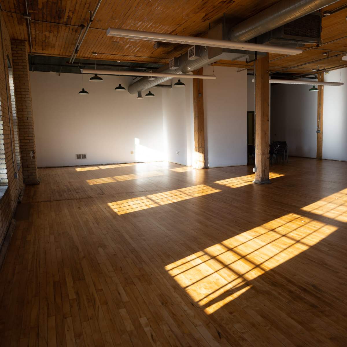 A spacious, empty room with wooden floors and large windows casting shadows on the surface.