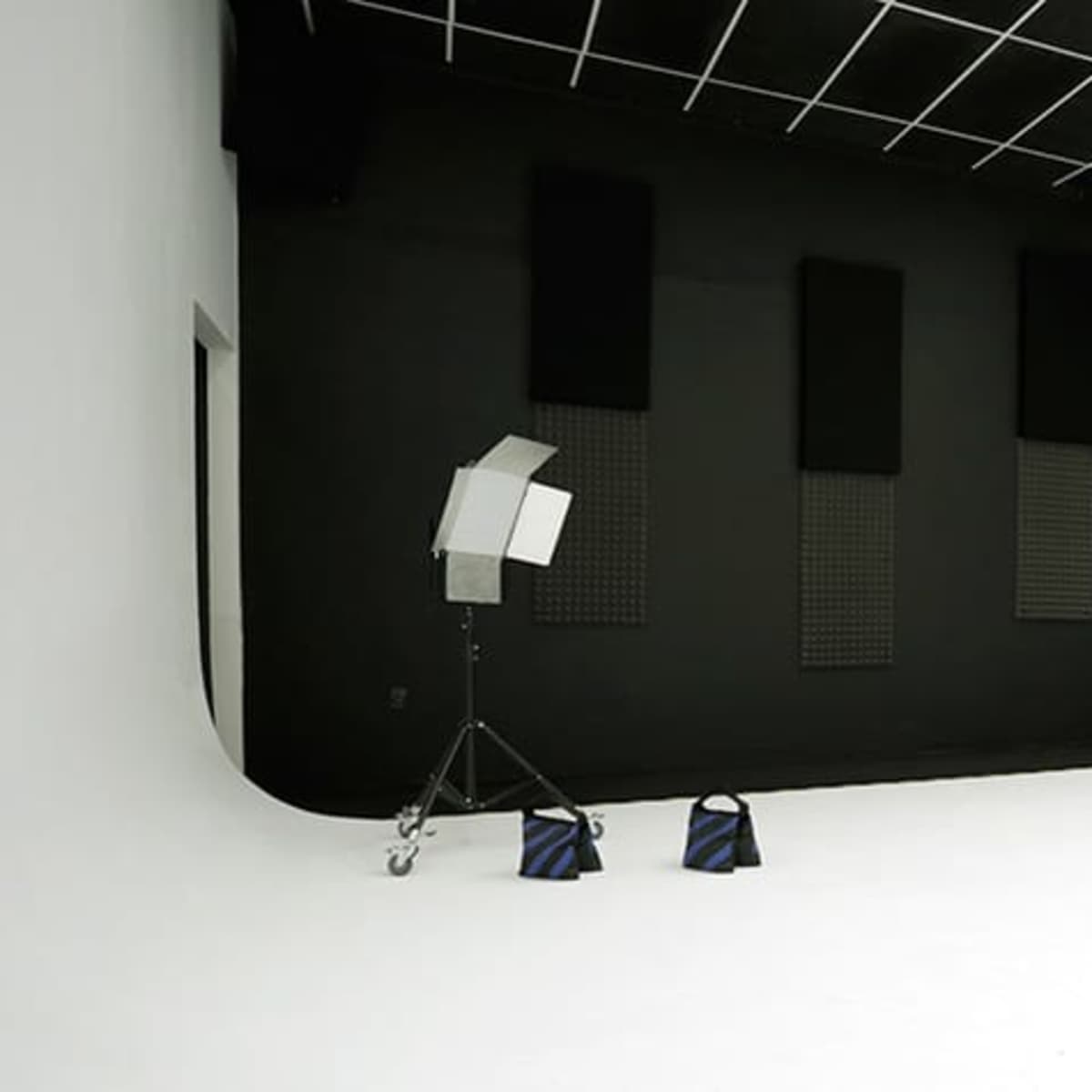 A spacious photo studio with a white backdrop, black walls, and various lighting equipment set up in the corner.