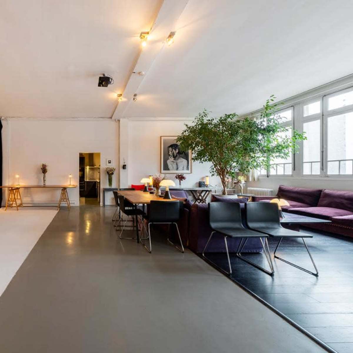 An open studio space with a black backdrop, a table with candles, a seating area with a purple sofa, and a large window letting in natural light.