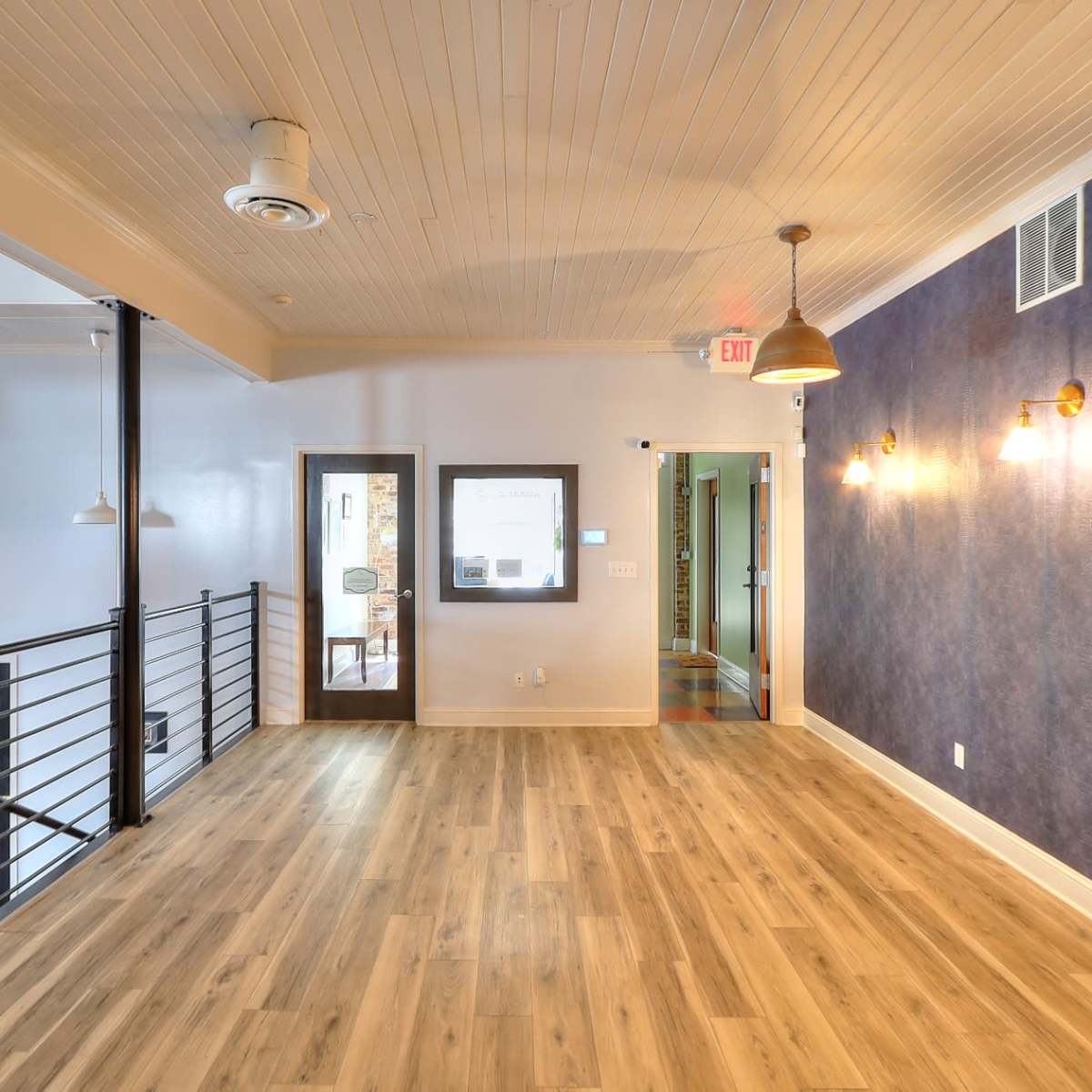 A spacious interior with wooden flooring, a blue accent wall, and various light fixtures, along with doors leading to other rooms.