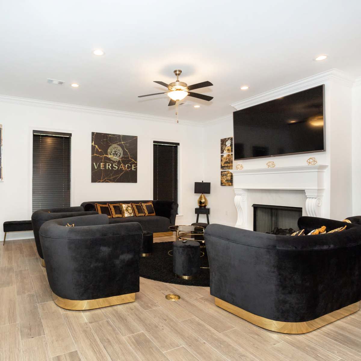 The living room features black velvet furniture with gold accents, a large flat-screen television, and a decorative fireplace.