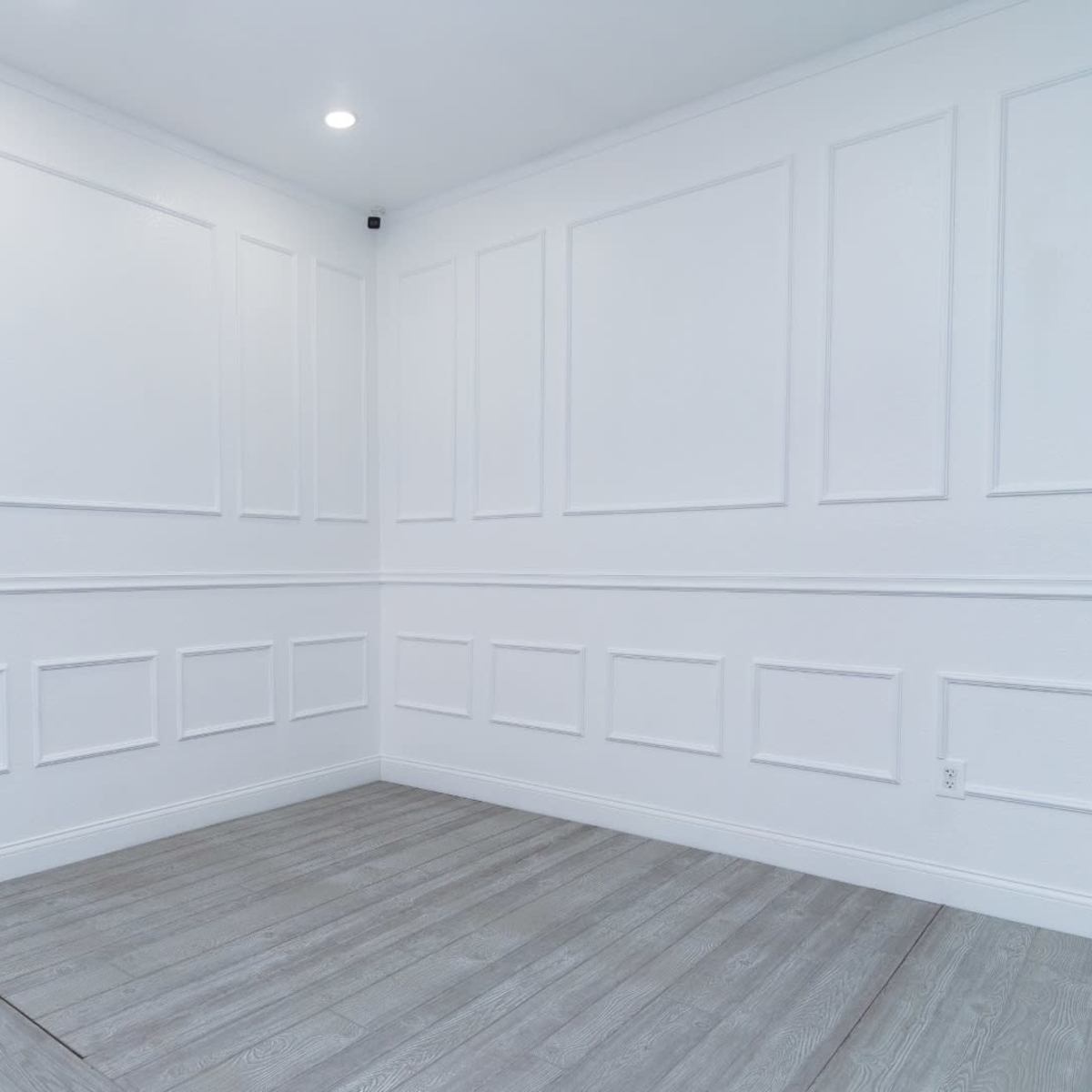 A empty room with white walls featuring decorative paneling and a light-colored floor.