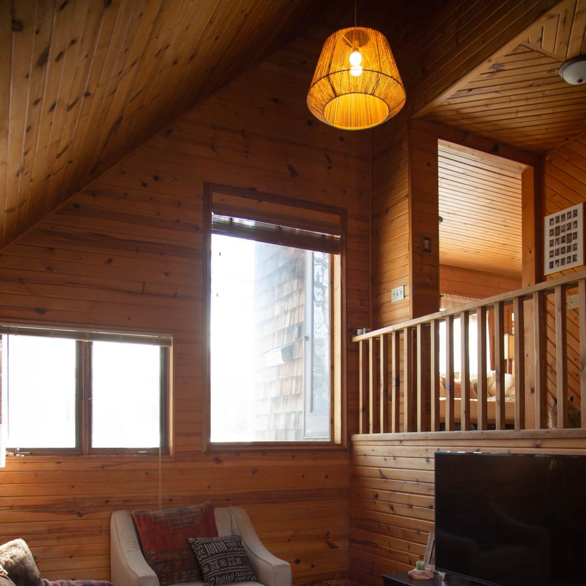 A wooden interior living space with a sofa, a coffee table, and a television, featuring a large window that lets in natural light.