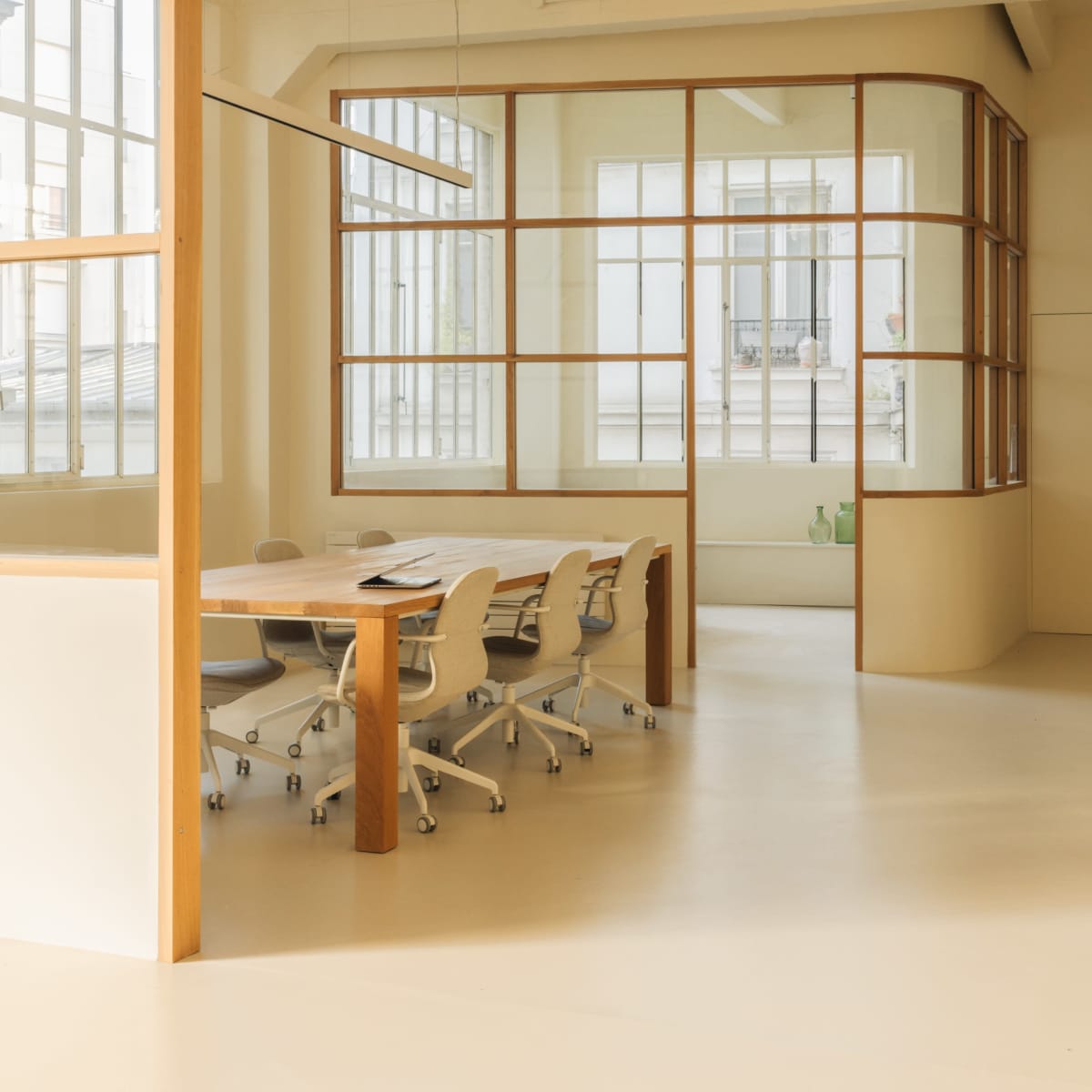 A modern conference room featuring a long wooden table surrounded by ergonomic chairs, with large windows providing natural light.