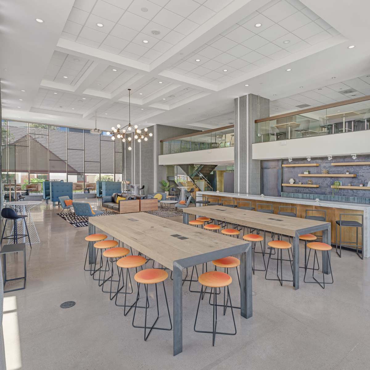 A spacious modern communal area featuring a large dining table with orange stools, a bar area, and various seating arrangements.