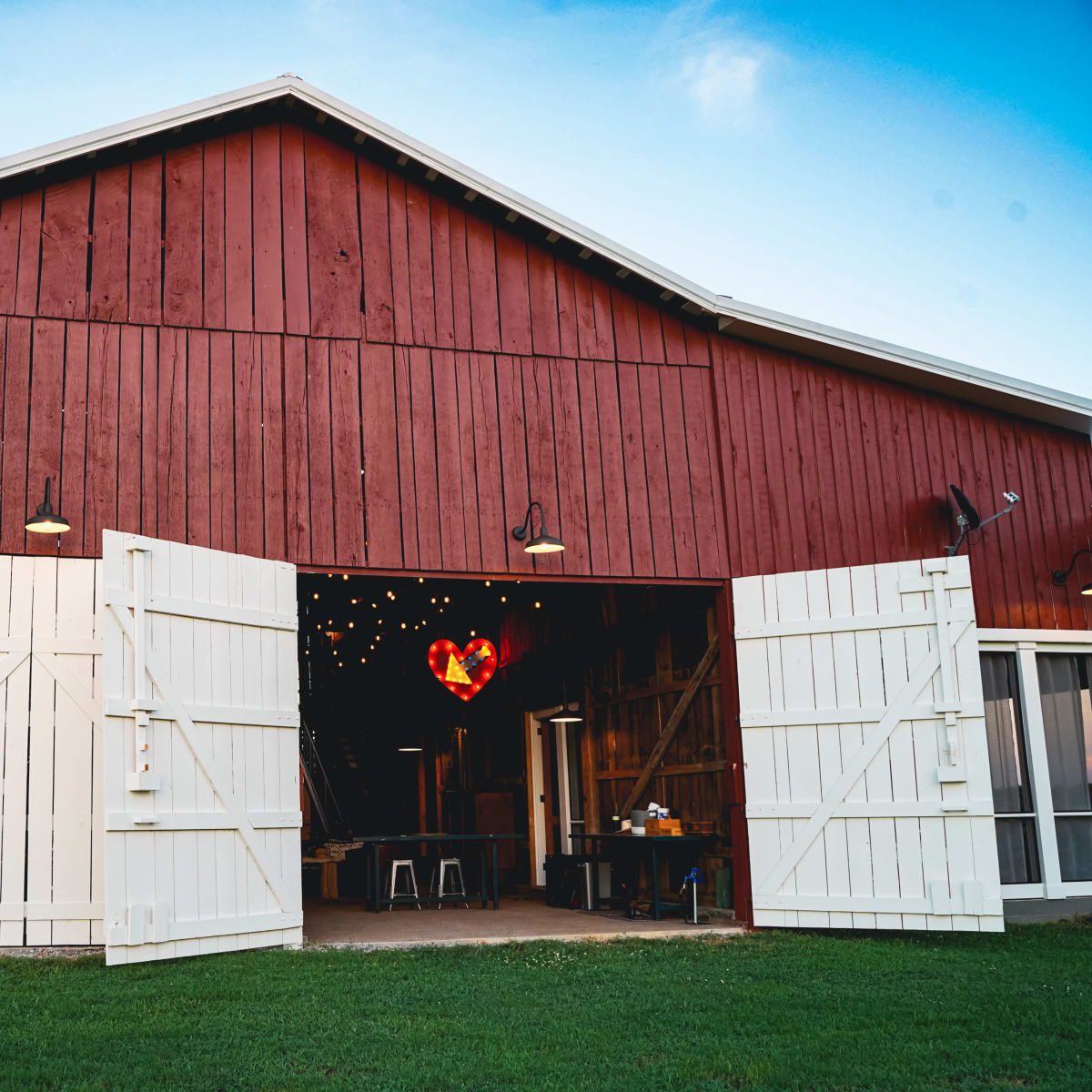 A red barn with white double doors is open, revealing a heart-shaped light fixture hanging inside.