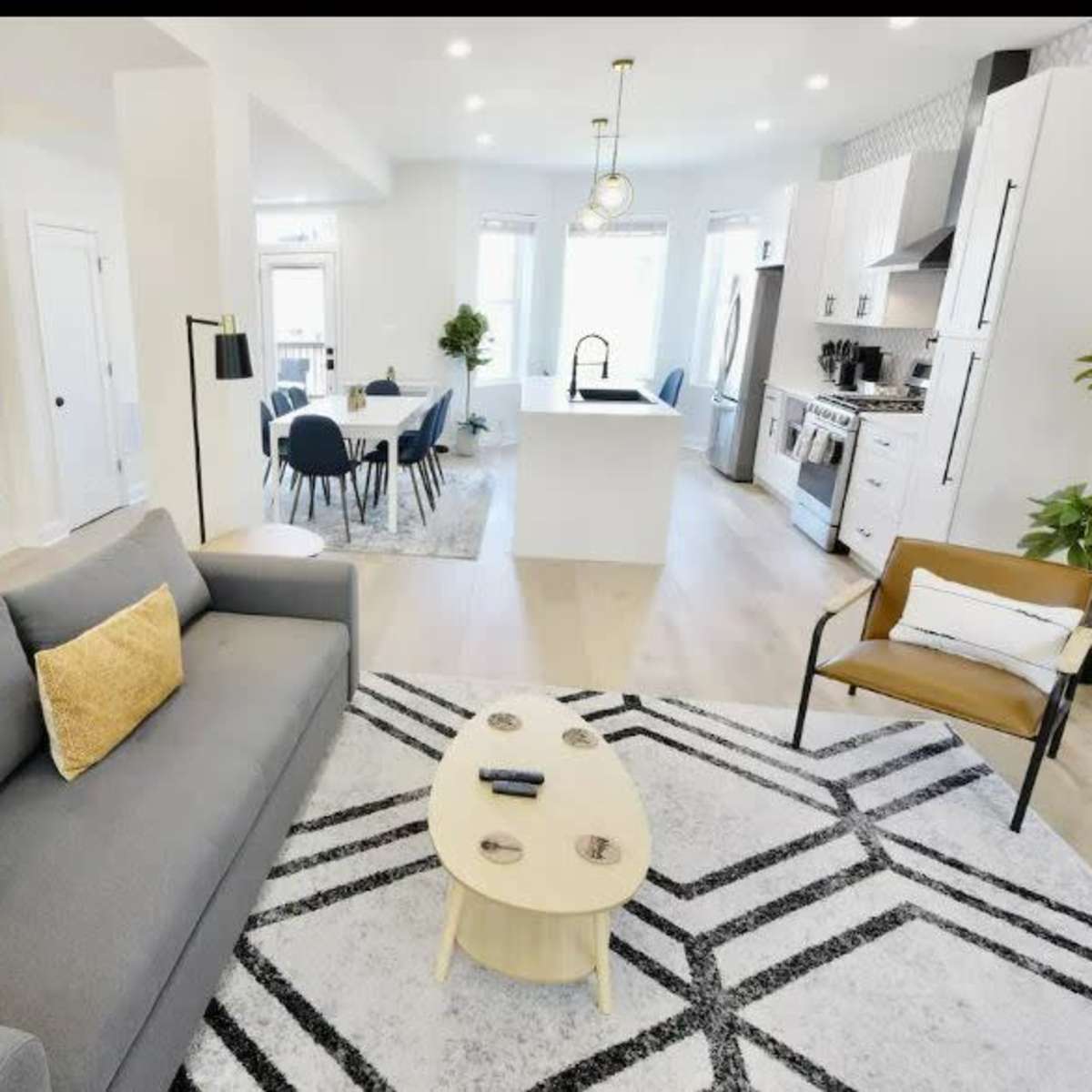 A modern living room featuring a gray sofa, a round coffee table, and a staircase, leading to a dining area with a kitchen in the background.
