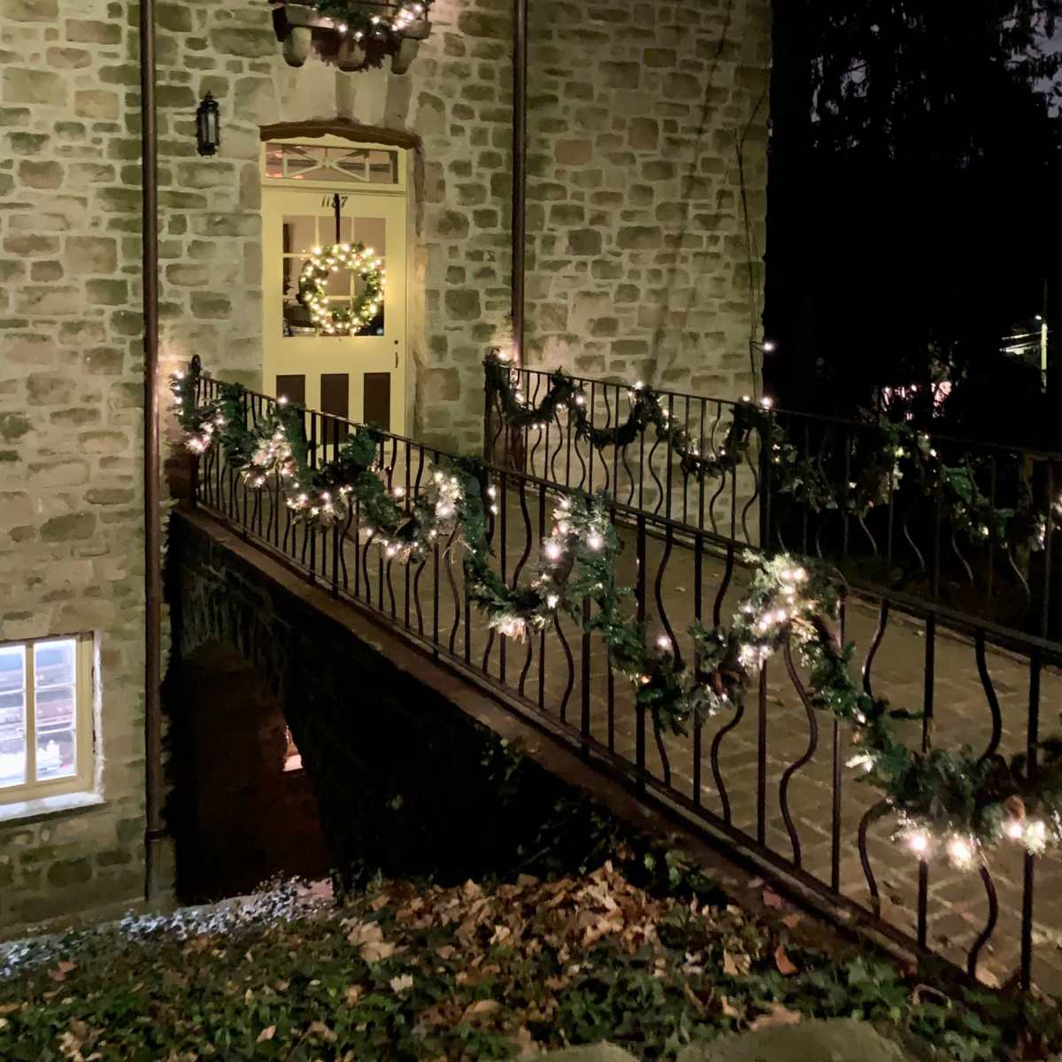 A stone building is illuminated at night with a decorated entrance and a railing adorned with garlands and lights.