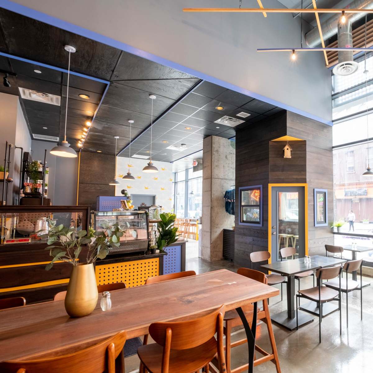 A modern café features large windows, wooden tables, and a sleek interior design with a view of the street outside.