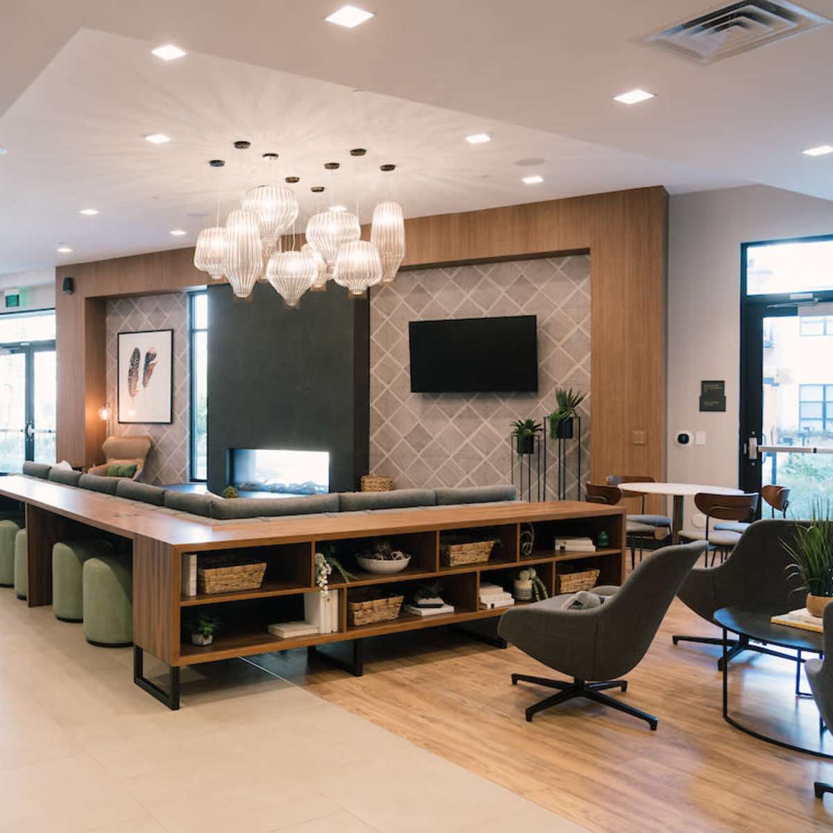 A modern lobby area featuring a long table with seating, a decorative fireplace, and a geometric accent wall.