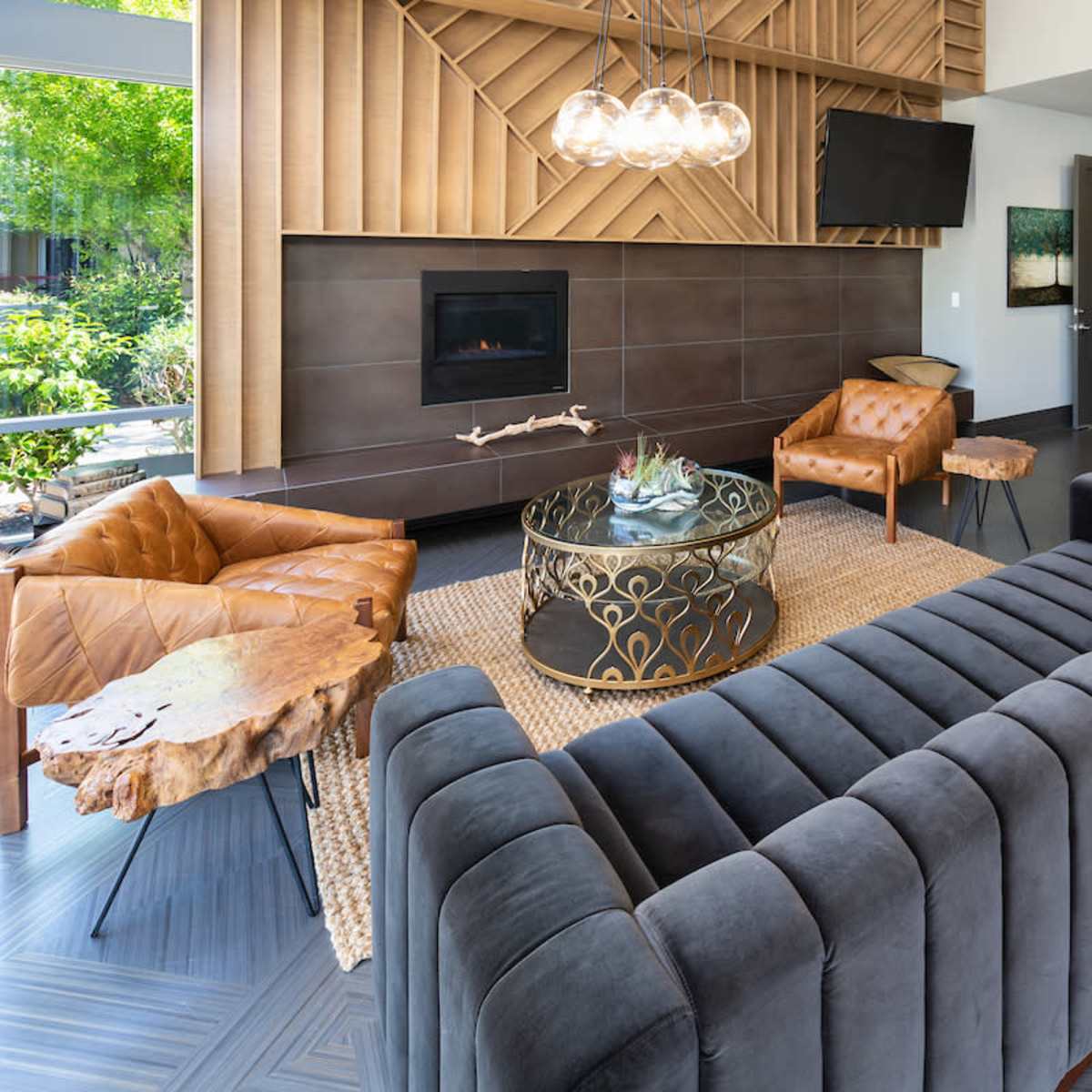 The living area features a modern design with a sectional sofa, leather chairs, a round coffee table, and a fireplace, all accentuated by large windows allowing natural light.