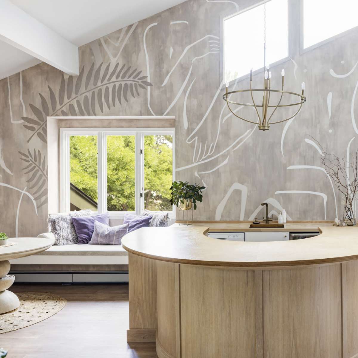 A modern kitchen with a curved wooden countertop, surrounded by a wall adorned with abstract white line art and a large window providing natural light.