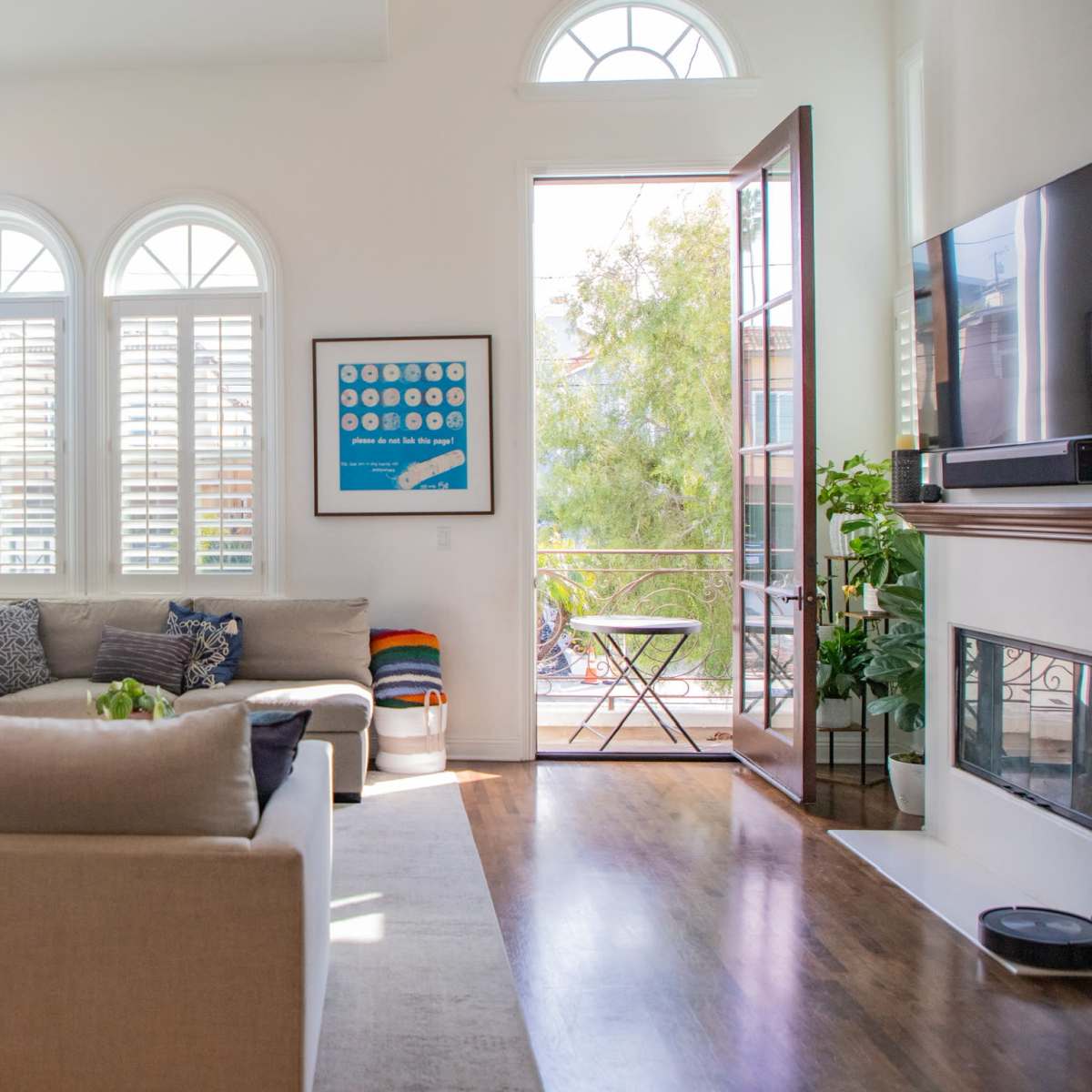 A bright living room features a large sectional sofa, art on the walls, and an open door leading to a balcony.