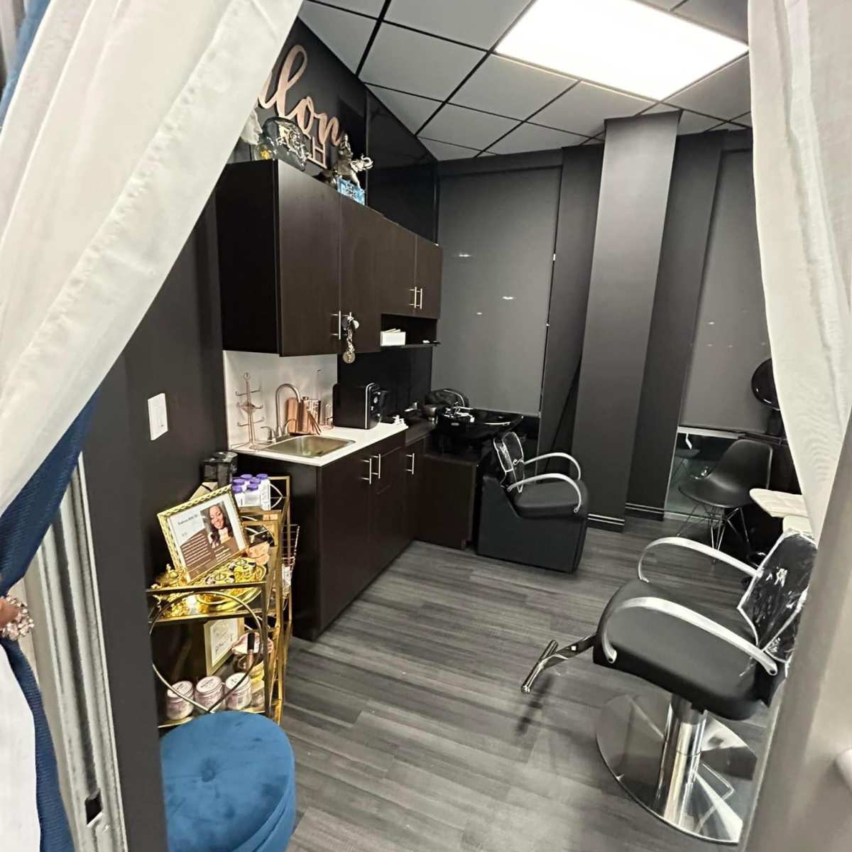 A small hair salon area with dark cabinetry, styling chairs, a waiting seat, and various hair care products displayed on a shelf.