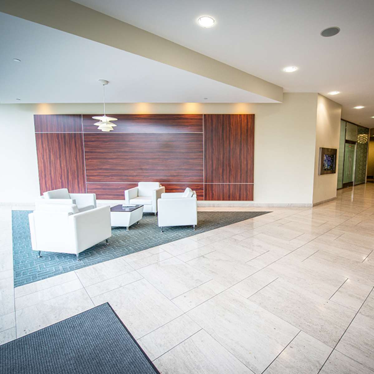 A modern lobby area with white seating, a wooden wall feature, and elevators in the background.