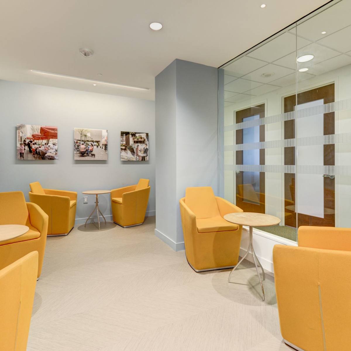 A small lounge area with orange chairs, side tables, and glass walls featuring framed photographs.