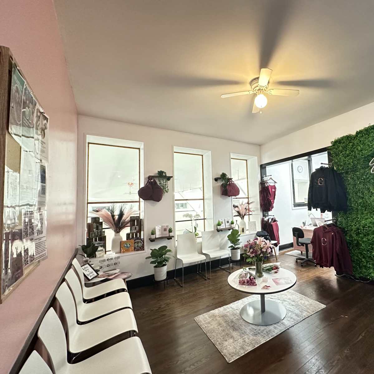 A dance studio's waiting area featuring a green moss wall, a circular coffee table, and seating arranged around the space with dance apparel displayed on hangers.