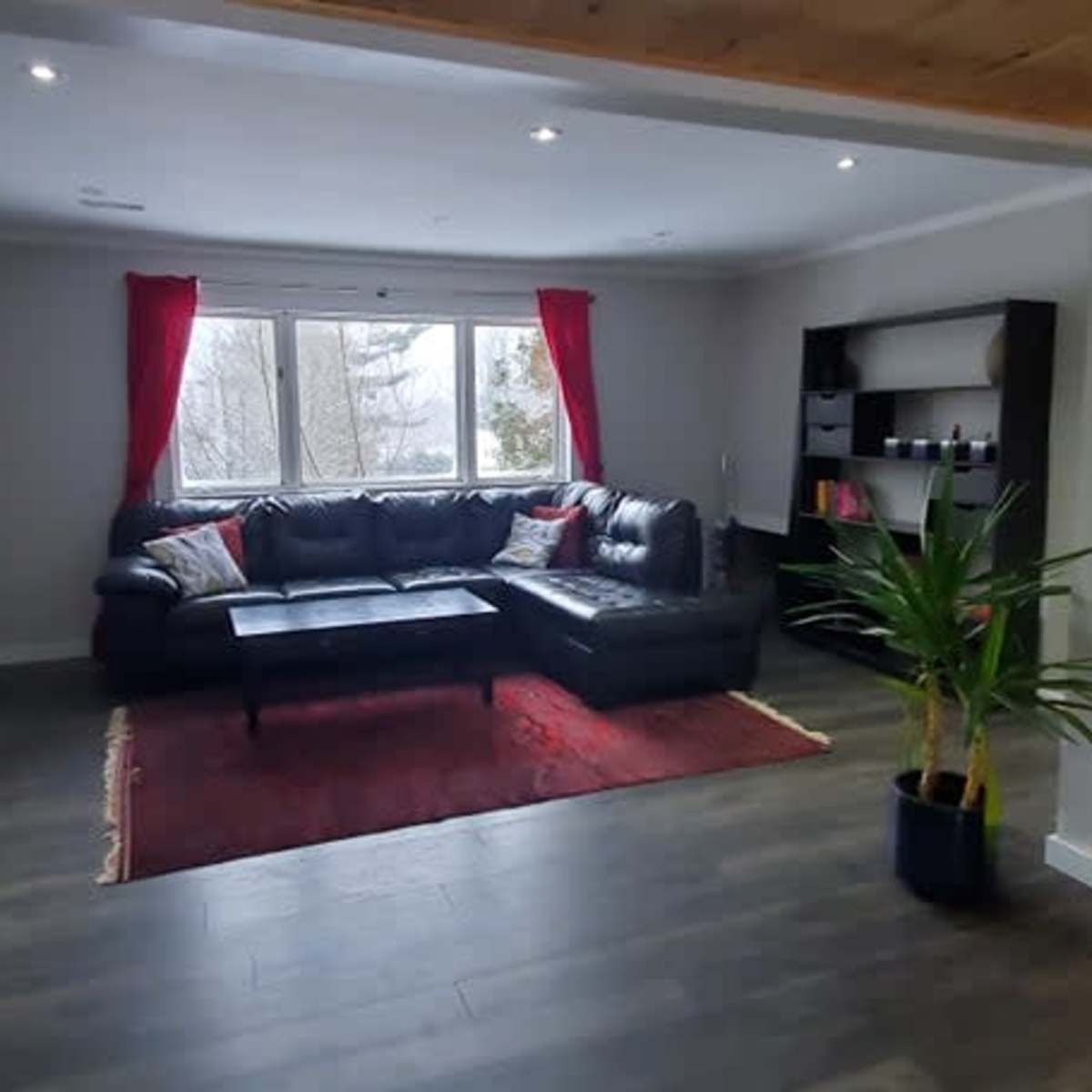 The living room features a black sectional couch, a coffee table on a red rug, and large windows with red curtains overlooking a snowy landscape.