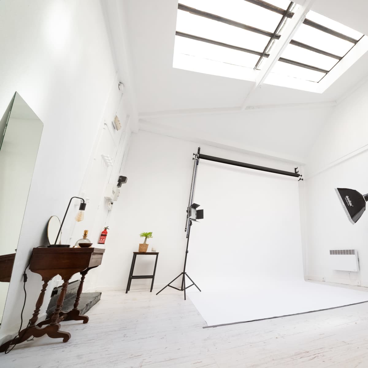 A bright photography studio features a white backdrop, lighting equipment, and minimal furnishings.