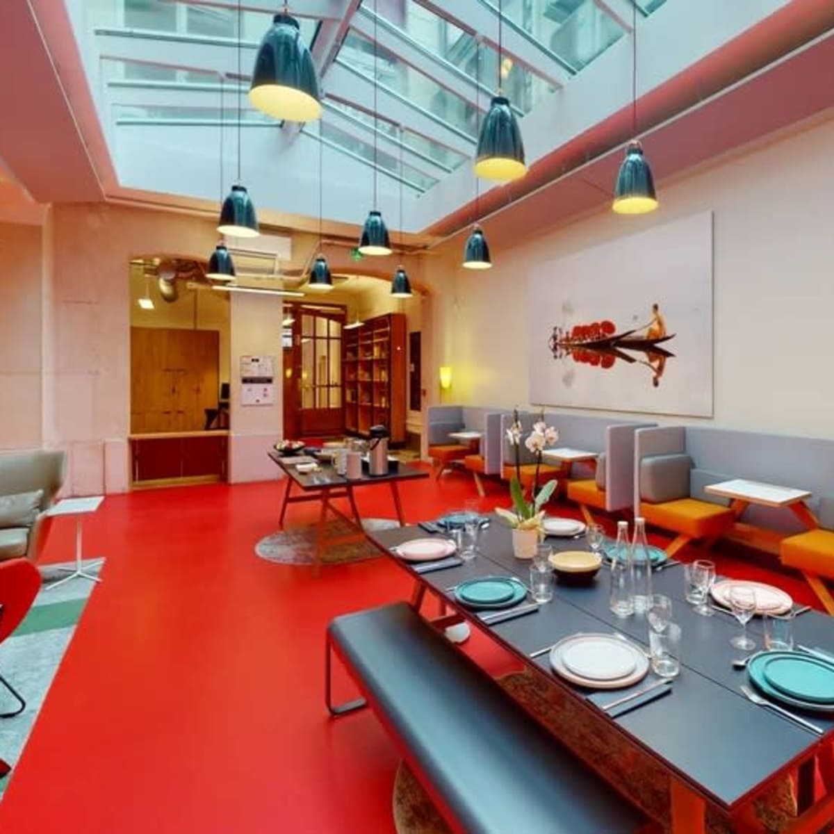A modern dining area with a large table set for a meal, surrounded by colorful chairs and illuminated by hanging lights.