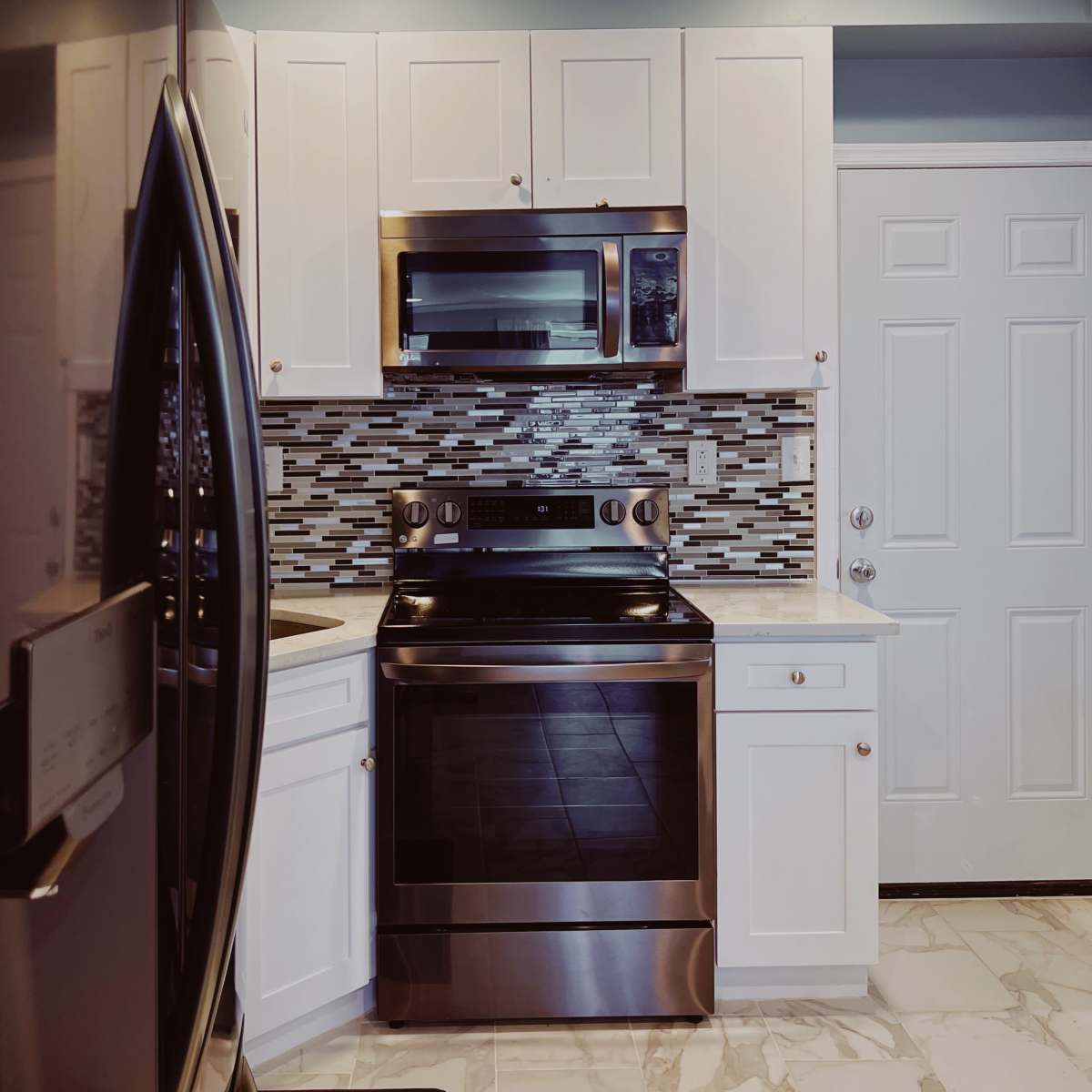 A modern kitchen features stainless steel appliances, white cabinetry, and a tiled backsplash.