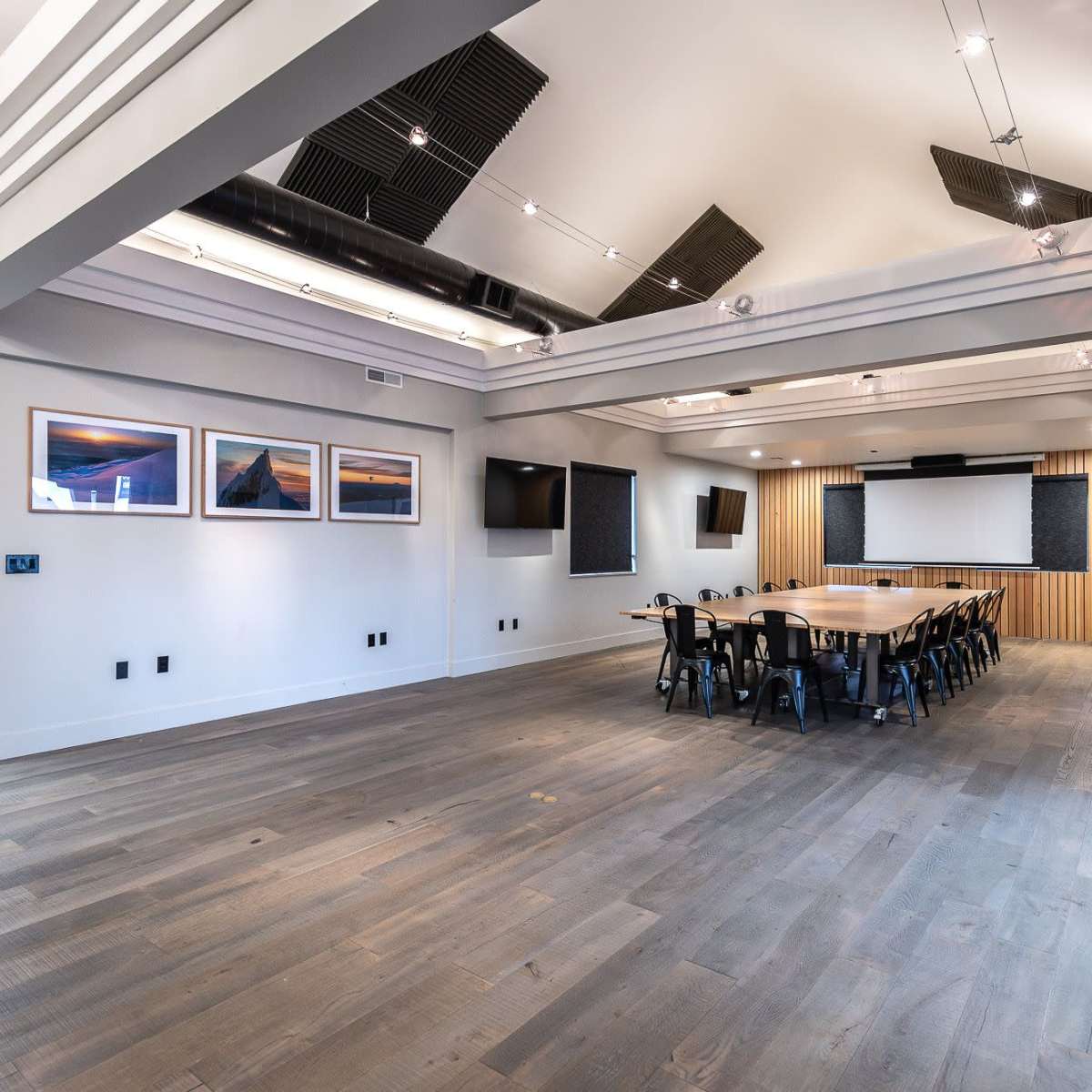 A modern conference room with a long table, several screens, and wooden paneling on the walls.