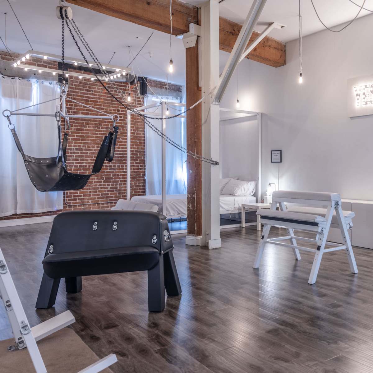 A spacious room with a bed, a swing chair, and modern furniture, featuring exposed brick walls and hanging light fixtures.