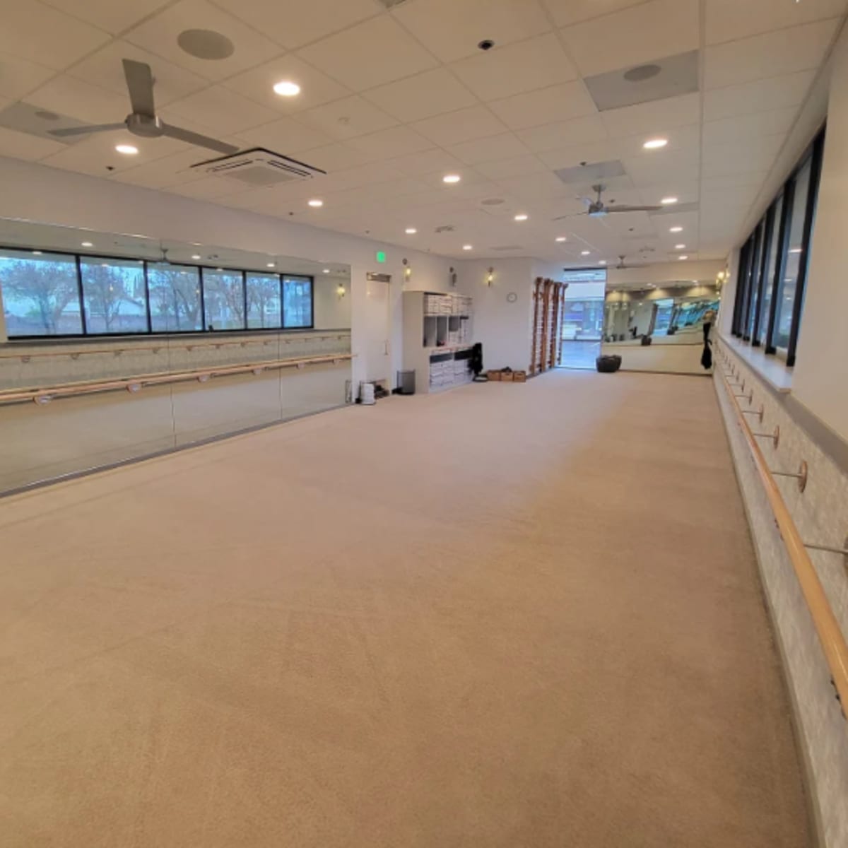 An empty fitness studio with mirrors along one wall and a barre installed across the room.