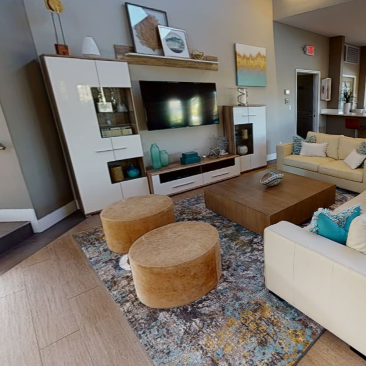 A modern living area with a white sofa, two round ottomans, a coffee table, and a television unit, all arranged around a patterned rug.