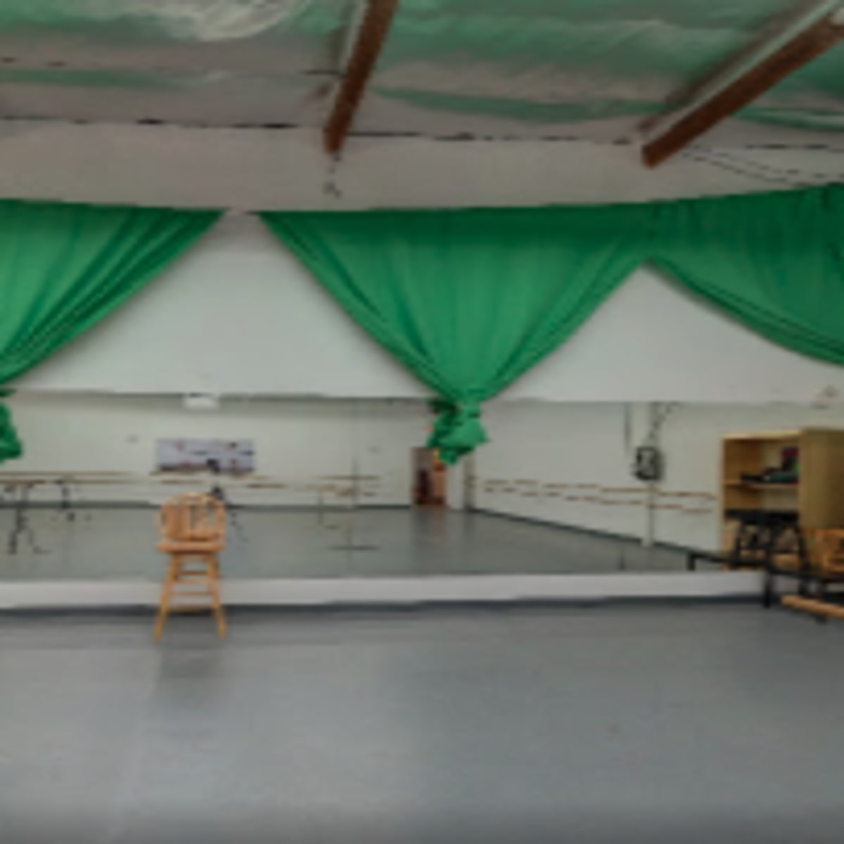 A dance studio with green drapes, a mirrored wall, and ballet barres along the sides.