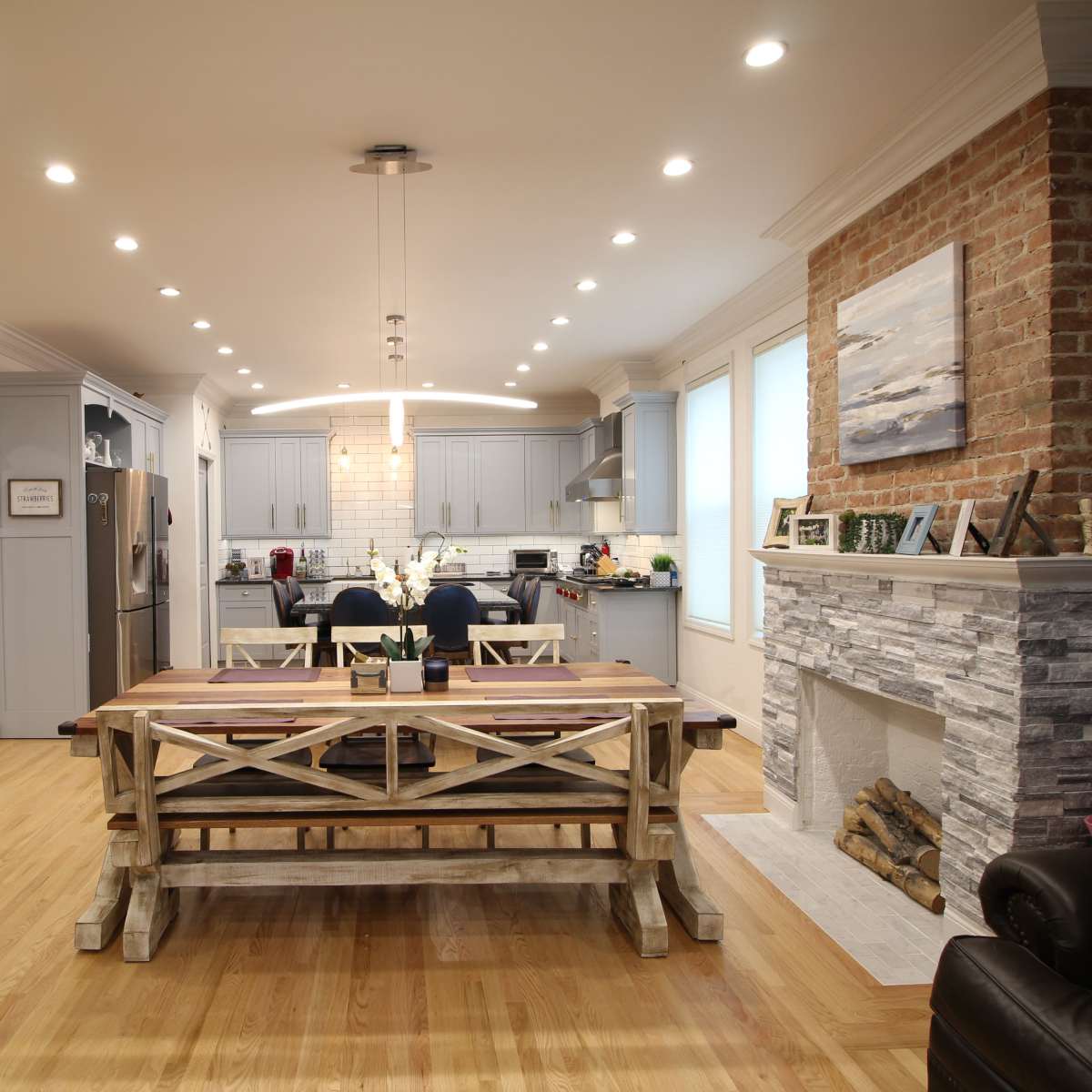 A modern open-concept kitchen and dining area featuring a wooden dining table, brick and stone accents, and a staircase leading to the upper level.
