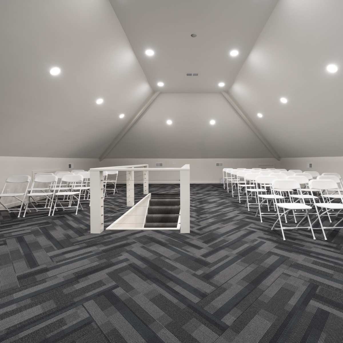 A spacious attic area with rows of white folding chairs arranged for an event, illuminated by recessed lighting.