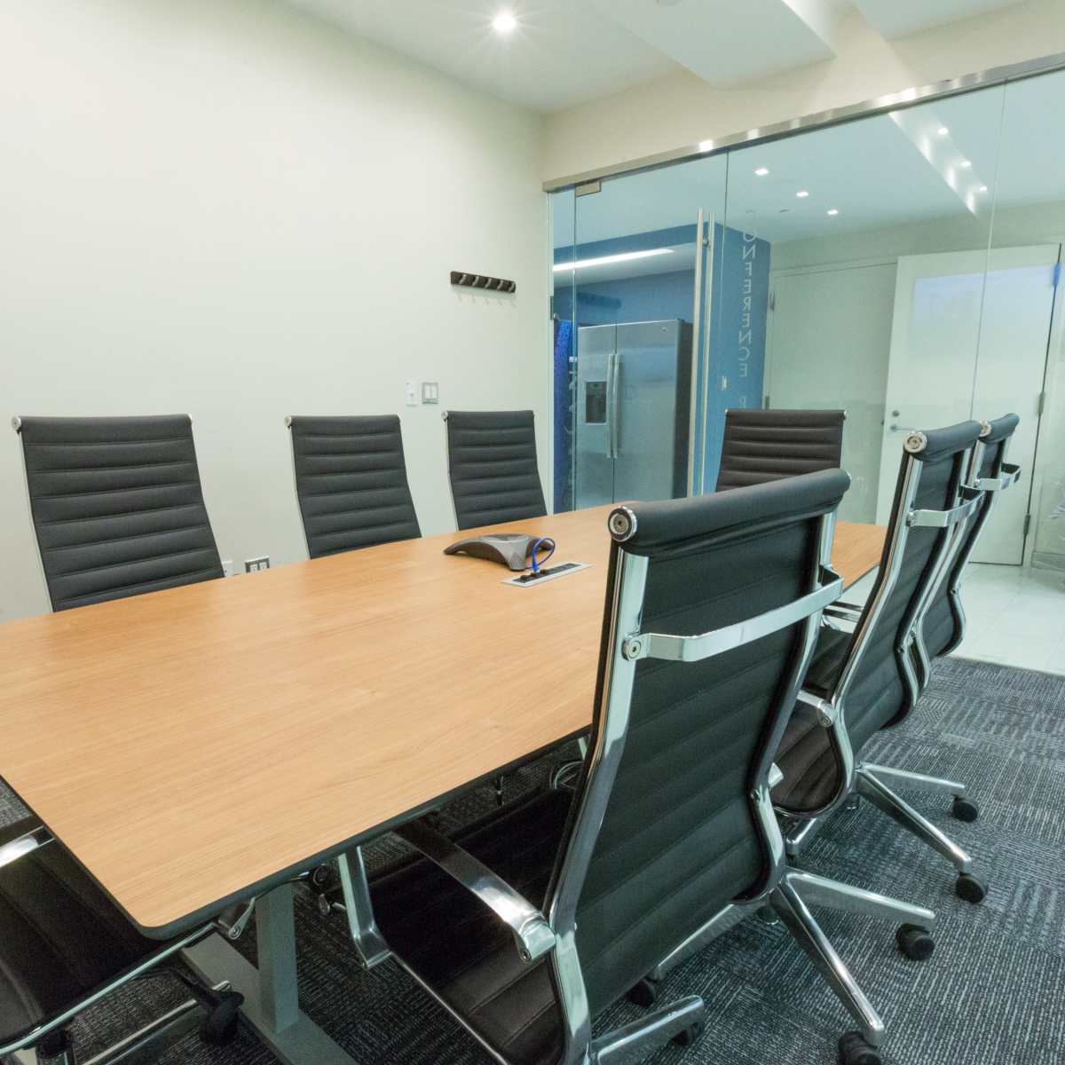 A modern conference room features a wooden table surrounded by black ergonomic chairs and a glass wall.