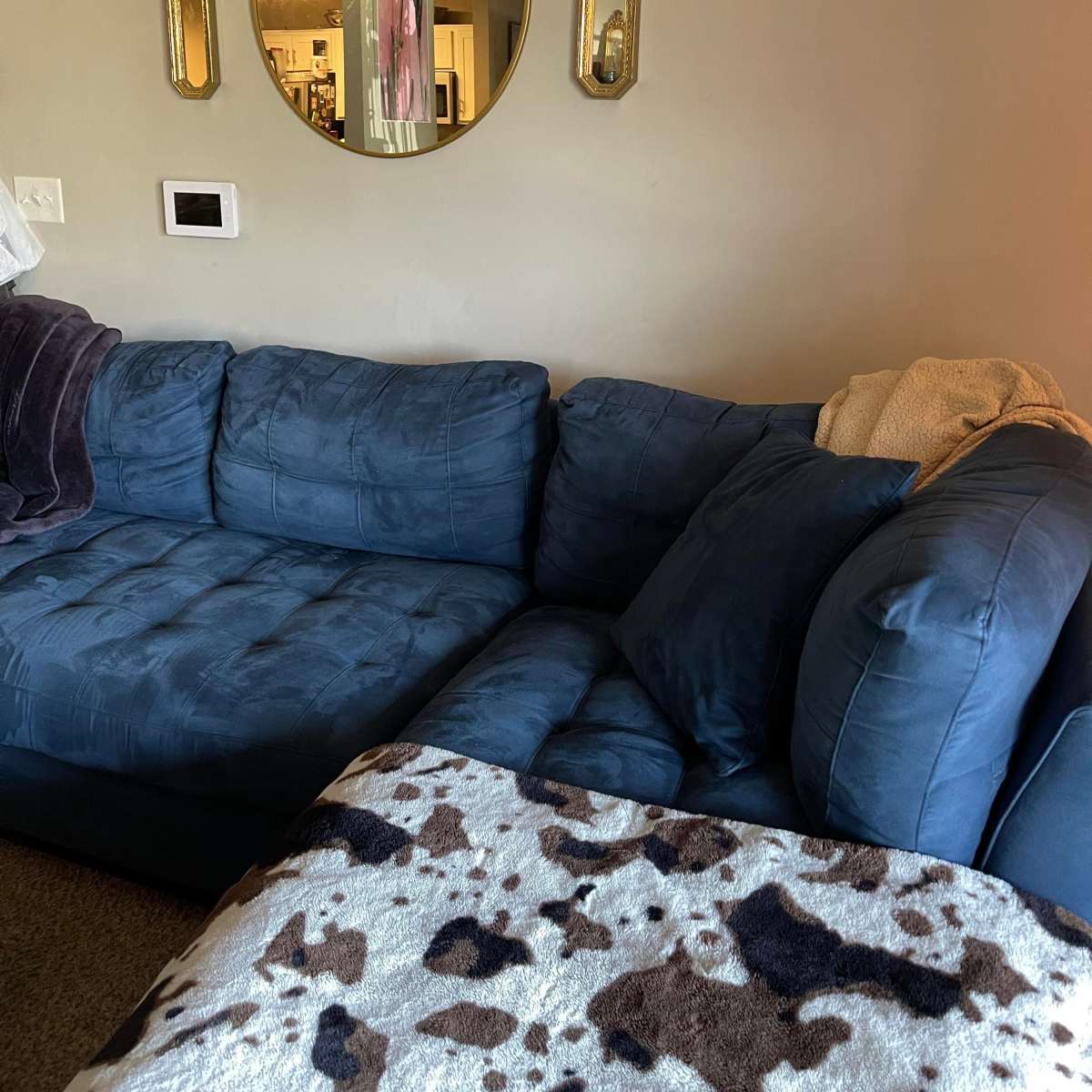 A blue sectional sofa in a living room with a round mirror and two wall sconces hanging above it.