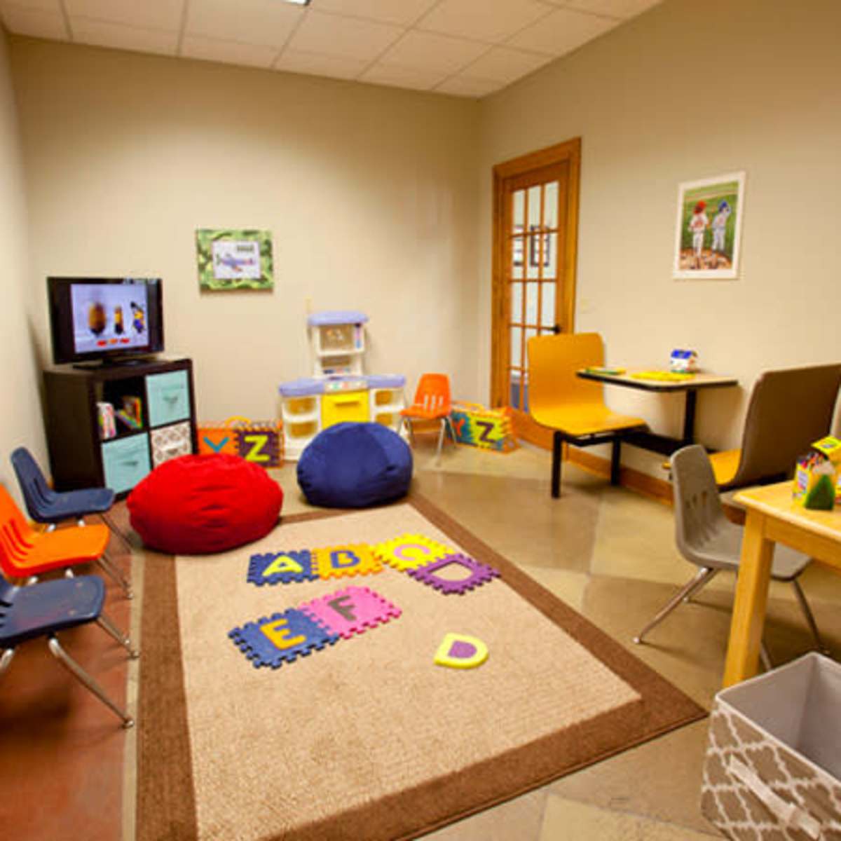A small, brightly colored children's playroom with a television, seating, and educational toys on the floor.